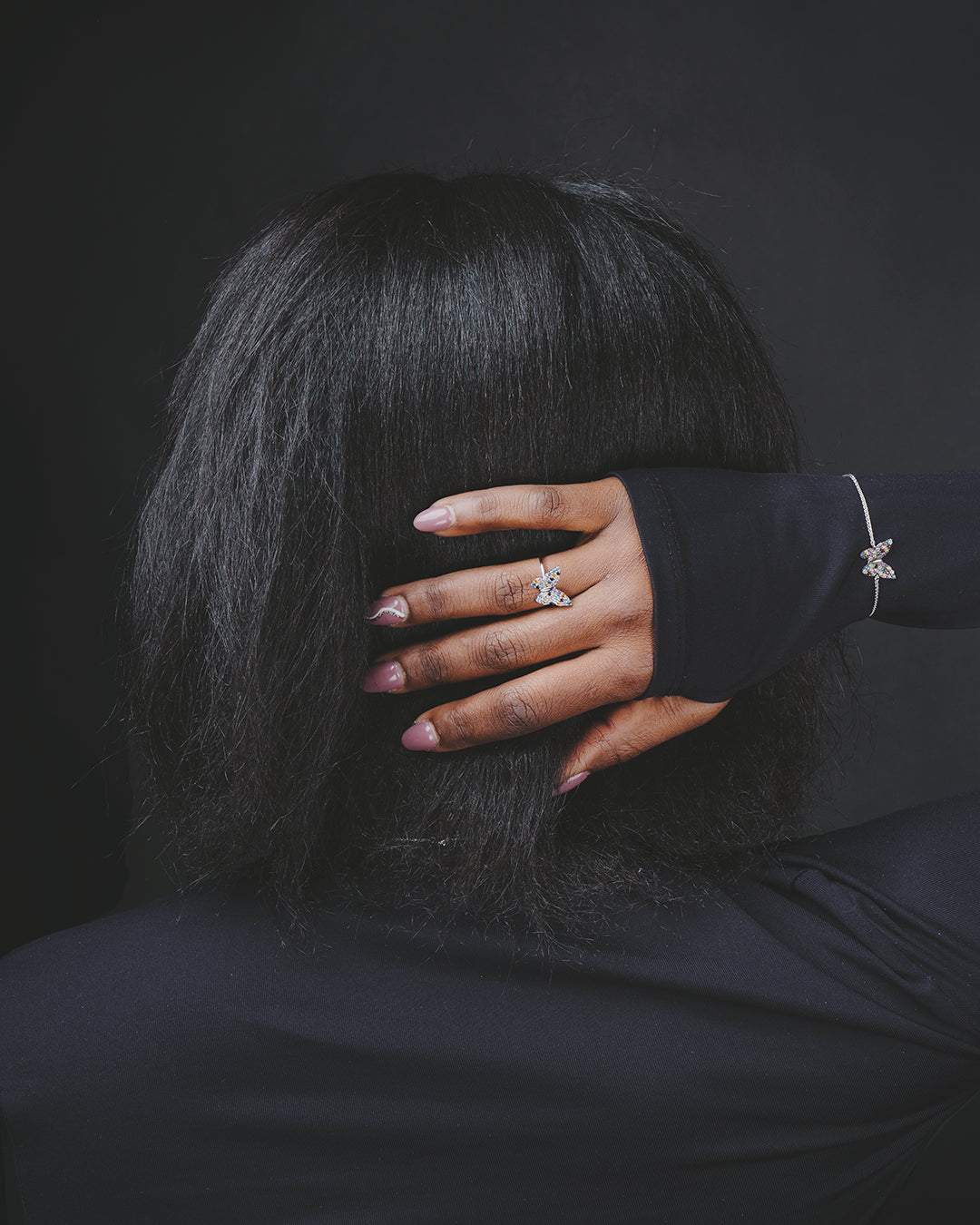 Modelo de espaldas con la mano en la cabeza enseñando el anillo de plata con un diseño de mariposa multicolor y la pulsera a juego