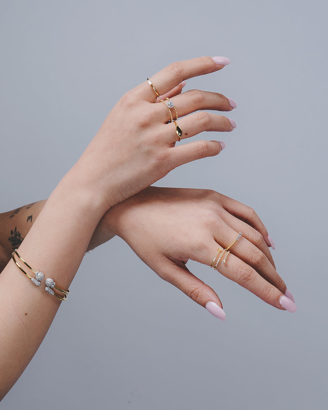 Manos sobre fondo gris donde se muestran varios anillos de la colección